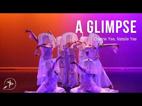 Dancers in white with veiled hats holding small lanterns, posed in a group against an orange-to-violet backdrop.